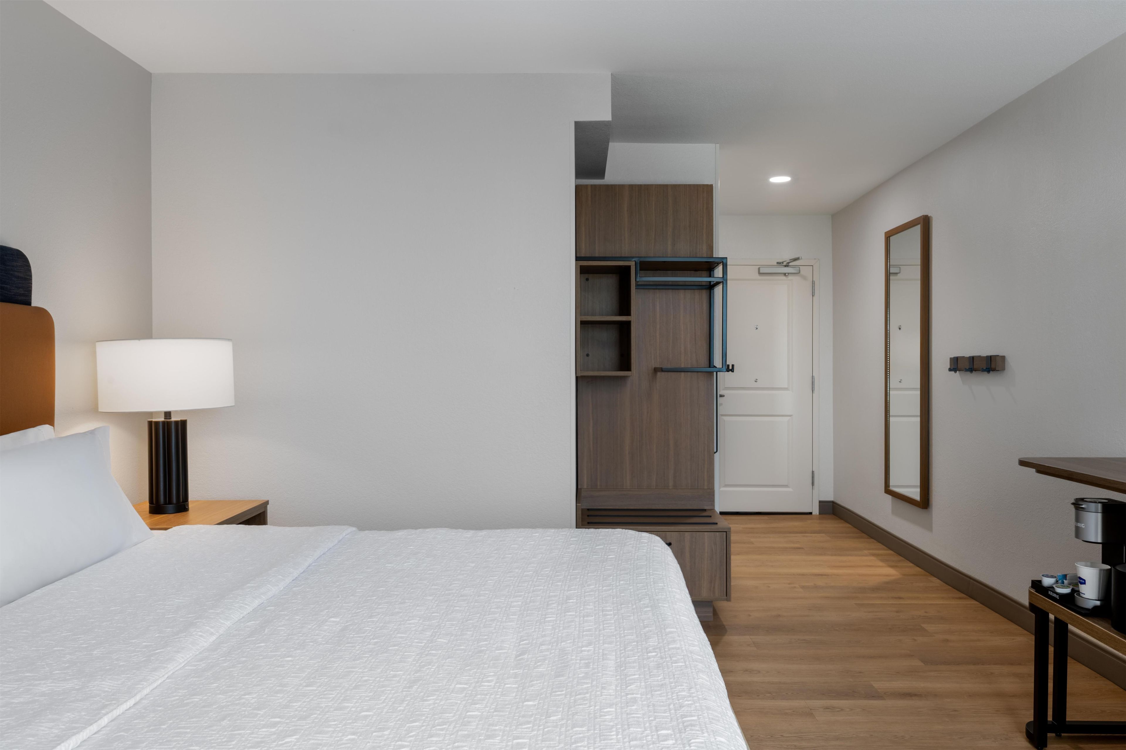 Una habitación de hotel con cama, mesita de noche, lámpara, armario y espejo.