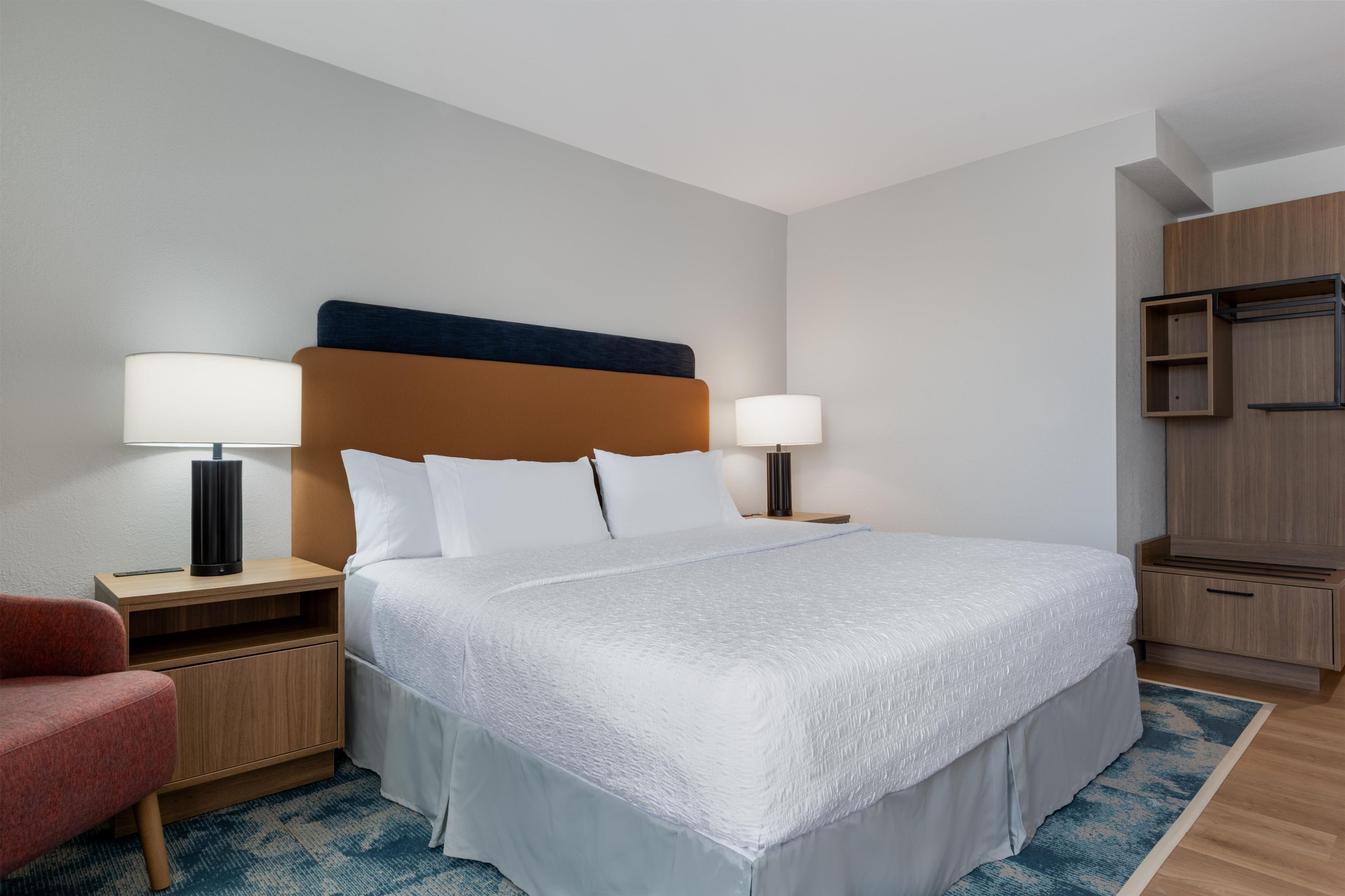A hotel room with a large bed, two bedside tables with lamps, a wooden wardrobe, and a red chair.