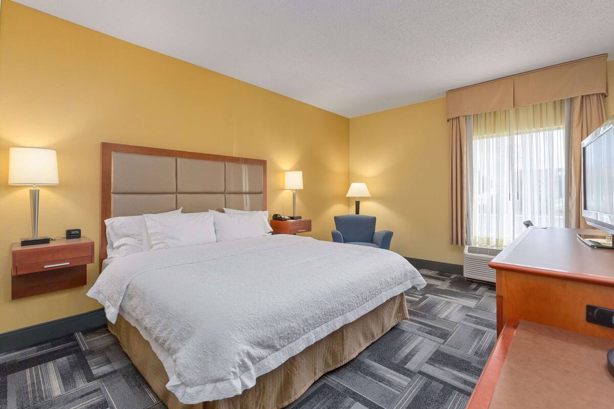 A hotel room with a large bed, two bedside tables with lamps, a desk, and a chair.