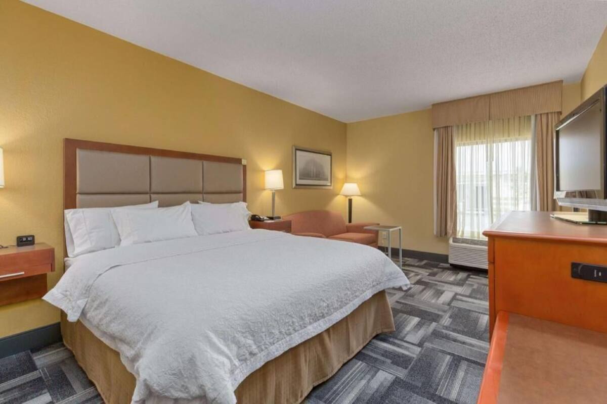 A hotel room with a large bed, a desk, a chair, a television, and a window with curtains.