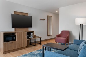A modern living room with a flat-screen TV, a coffee maker, a red armchair, a blue sofa, and a floor lamp. - Hampton Inn Owensboro South (Owensboro)