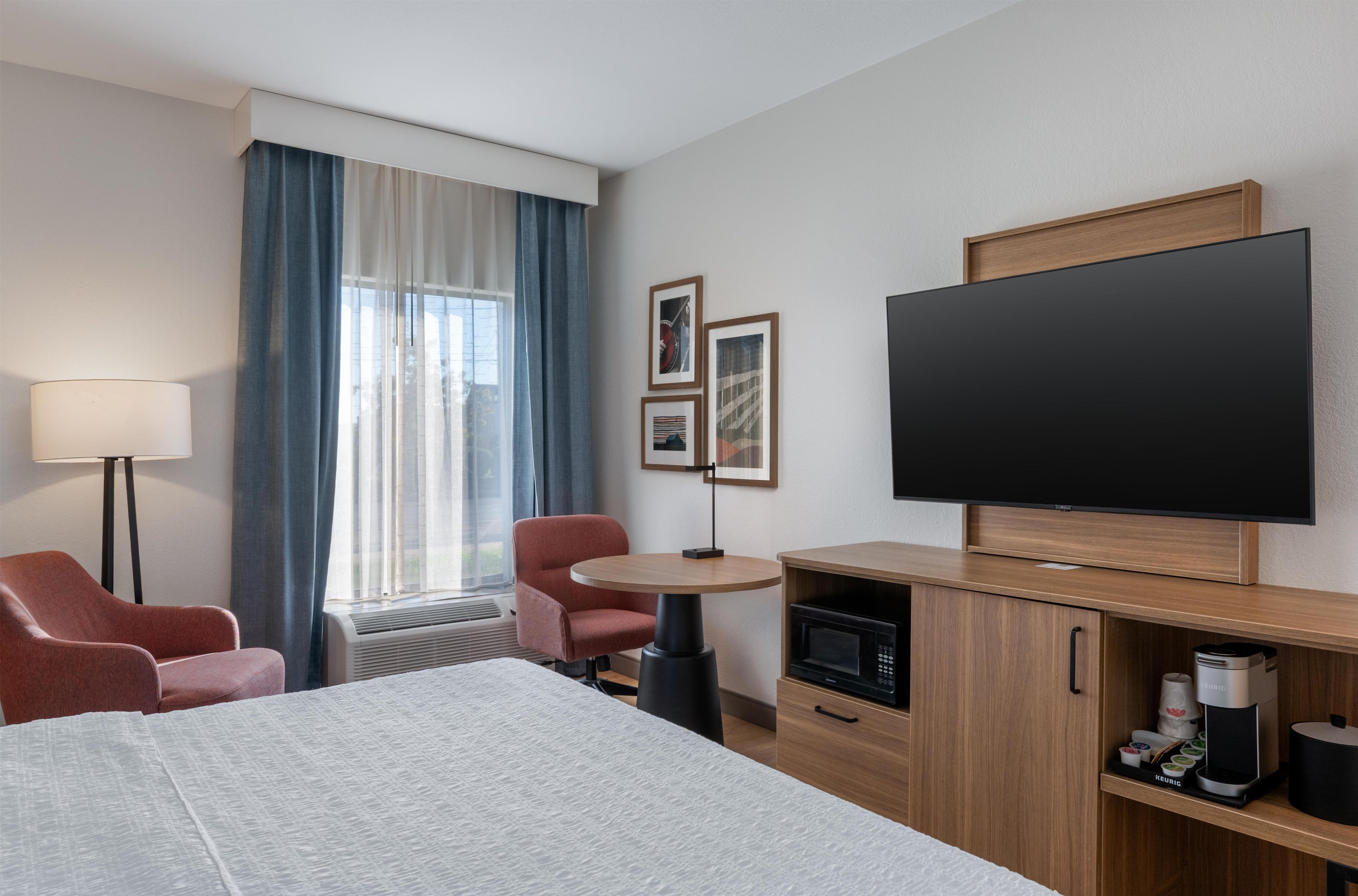 Una camera d'albergo con un letto, una scrivania, una sedia, un televisore e un mini-frigo.