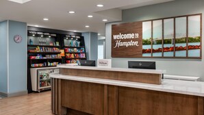 A hotel reception area with a wooden reception desk, a clock on the wall, and a vending machine stocked with snacks and drinks. - Hampton Inn Owensboro South (Owensboro)