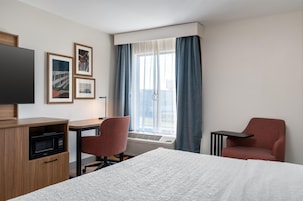 Una habitación de hotel con cama, escritorio, silla, televisión y ventana con cortinas.