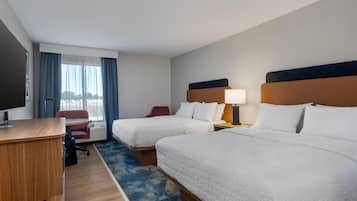 Habitación de hotel con dos camas, un escritorio, una silla, un televisor y una ventana con cortinas.