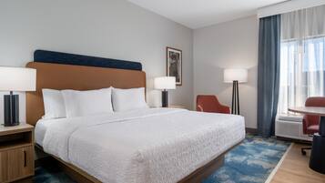 A hotel room with a large bed, two bedside tables, a desk, a chair, a lamp, and a window with curtains.