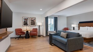 A hotel room with a bed, a sofa, two armchairs, a small table, a TV, and artwork on the walls. - Hampton Inn Owensboro South (Owensboro)
