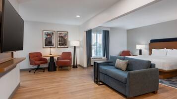 A hotel room with a bed, a sofa, two armchairs, a desk, a flat-screen TV, and two framed pictures on the wall.