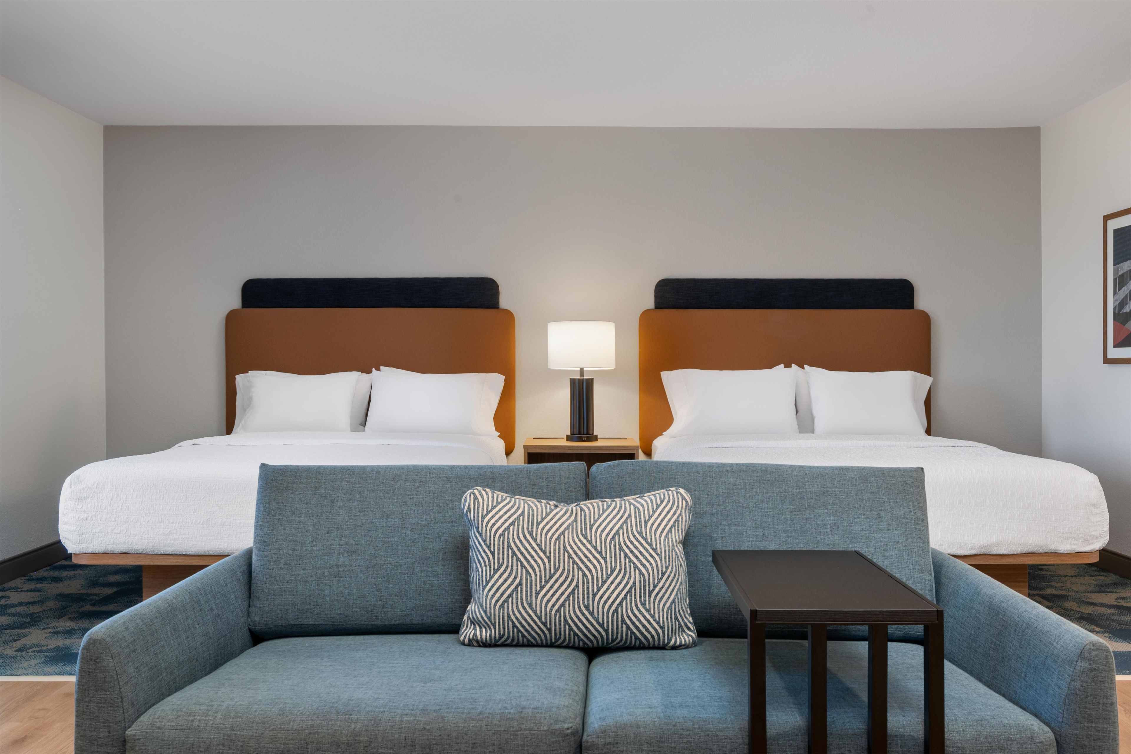 A hotel room with two beds, a sofa, a table, and a lamp.