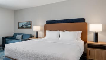 A hotel room with a large bed, two bedside tables with lamps, a blue sofa, and a framed picture on the wall.