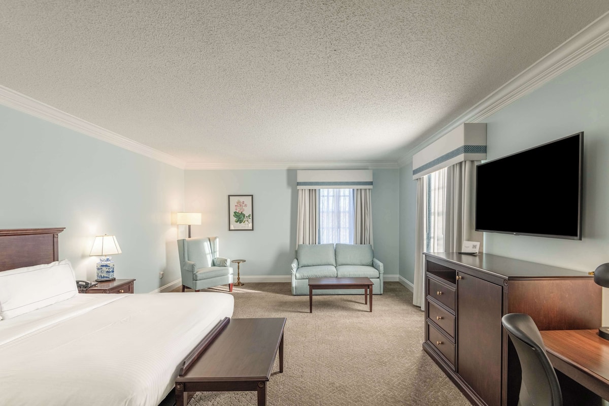 A hotel room with a bed, a desk, a chair, a TV, and a window with curtains.