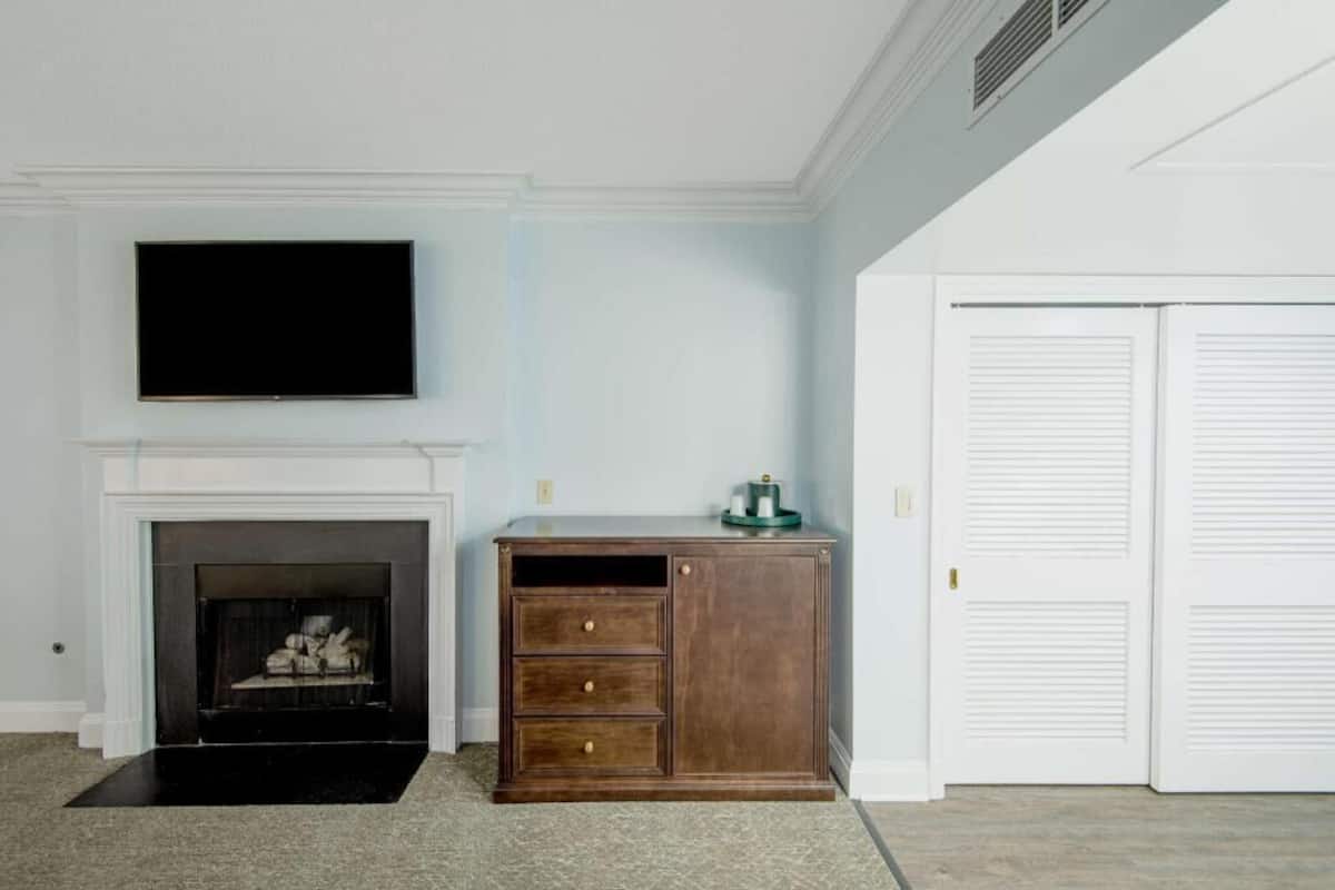 A room with a fireplace, a television mounted above it, a cabinet with drawers, and a set of white doors.