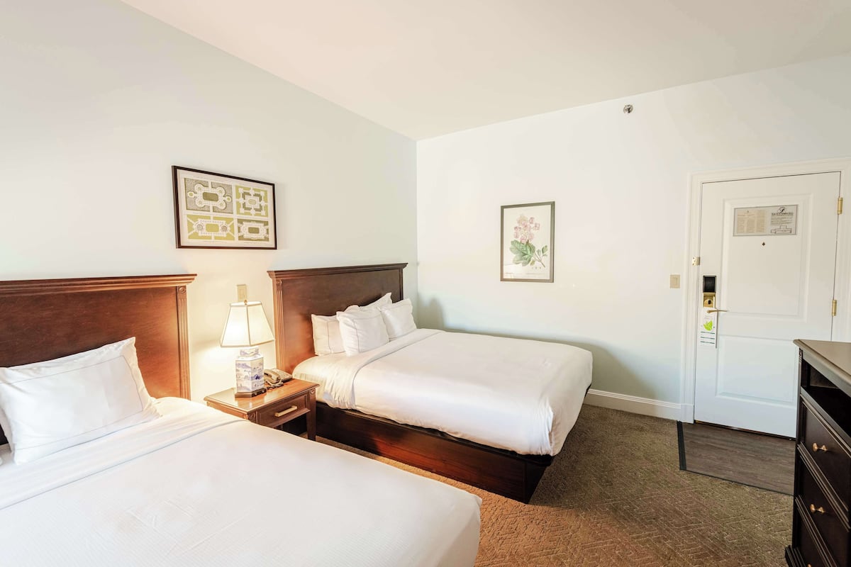 A hotel room with two beds, a nightstand with a lamp, a dresser, and framed pictures on the walls.