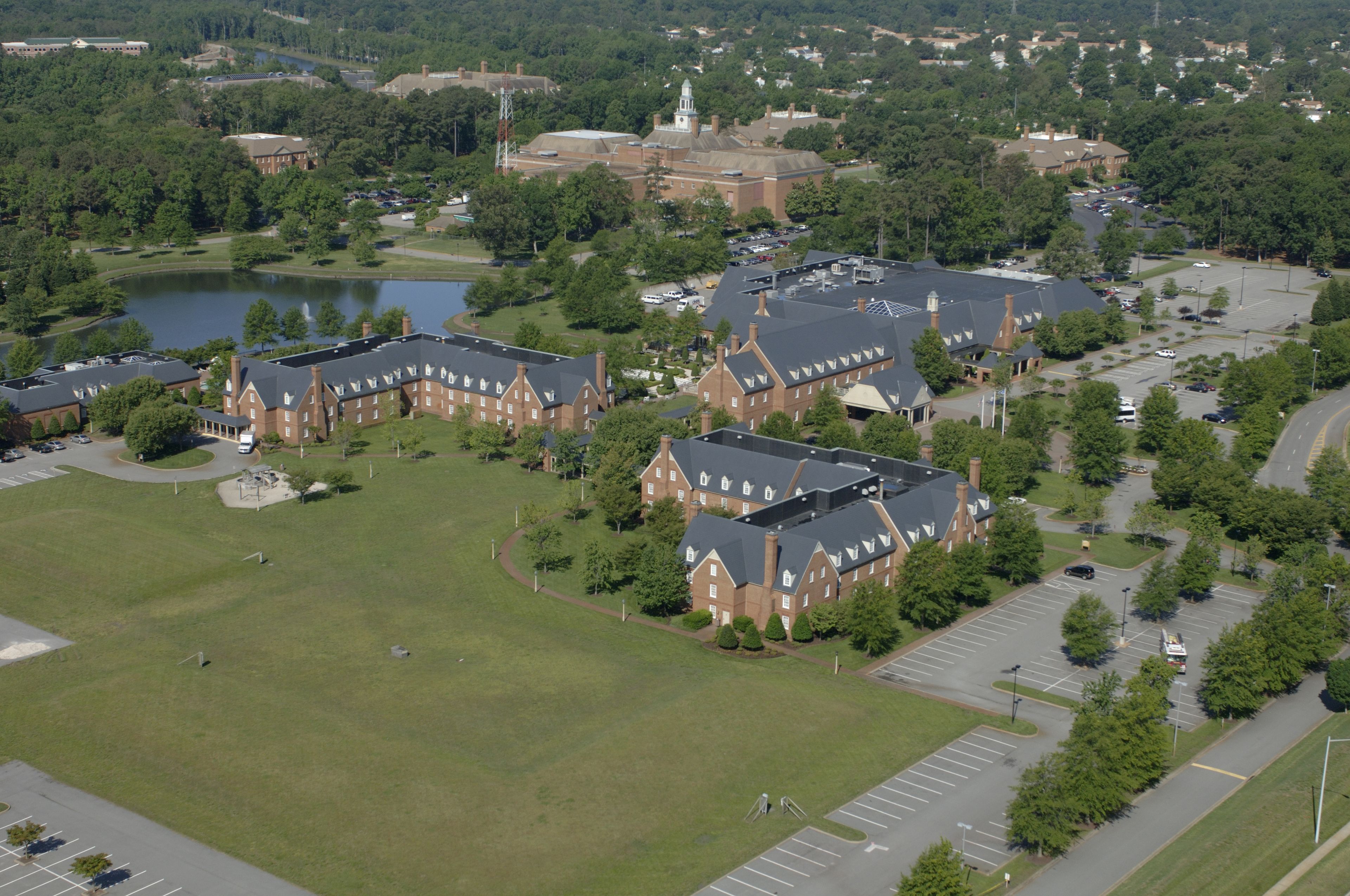 An aerial view of a campus with multiple buildings, a large green field, and a body of water.