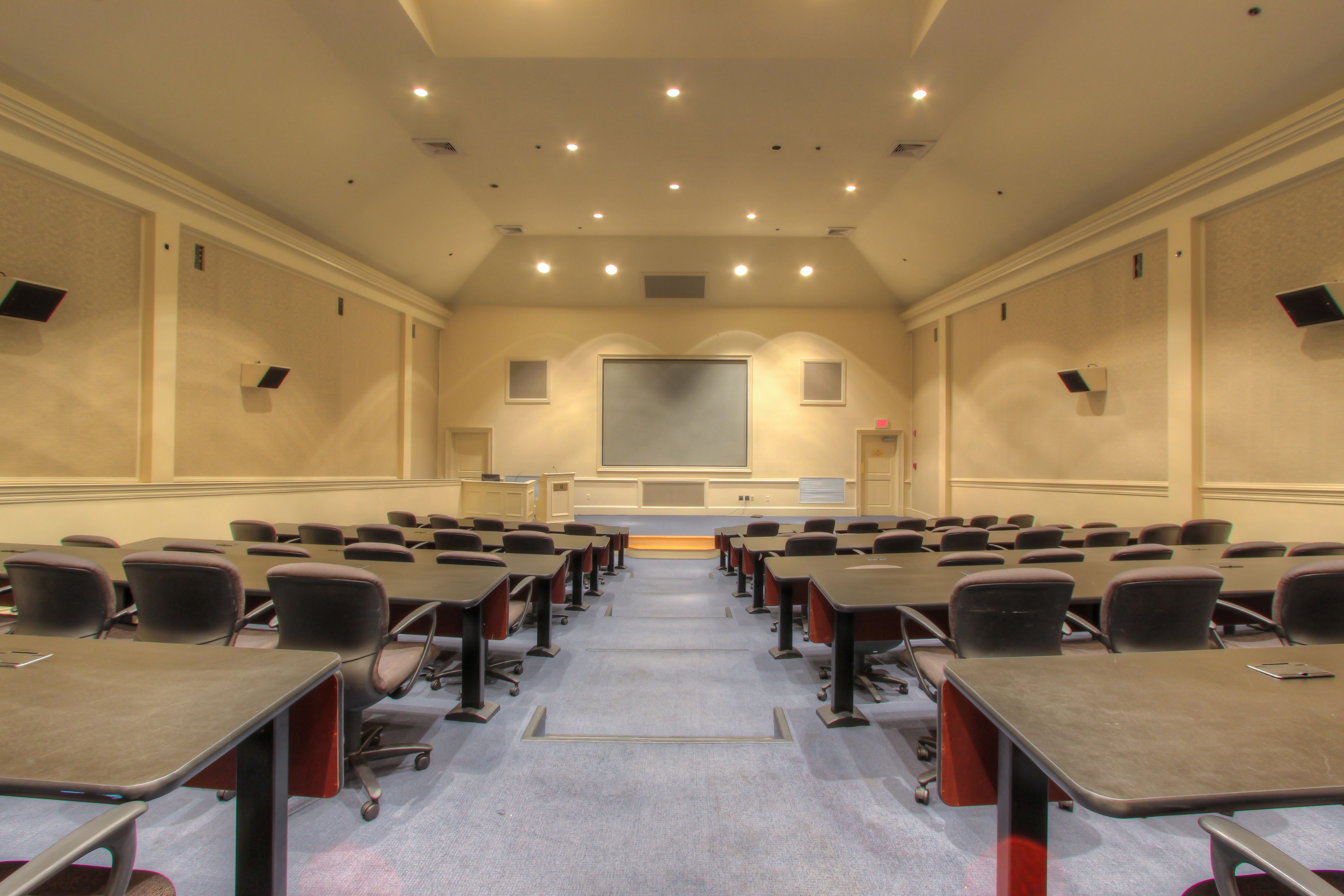 A conference room with rows of tables and chairs, a large screen, and a projector.