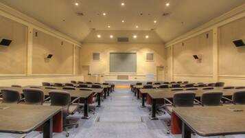 A conference room with rows of tables and chairs, a large screen, and a projector.