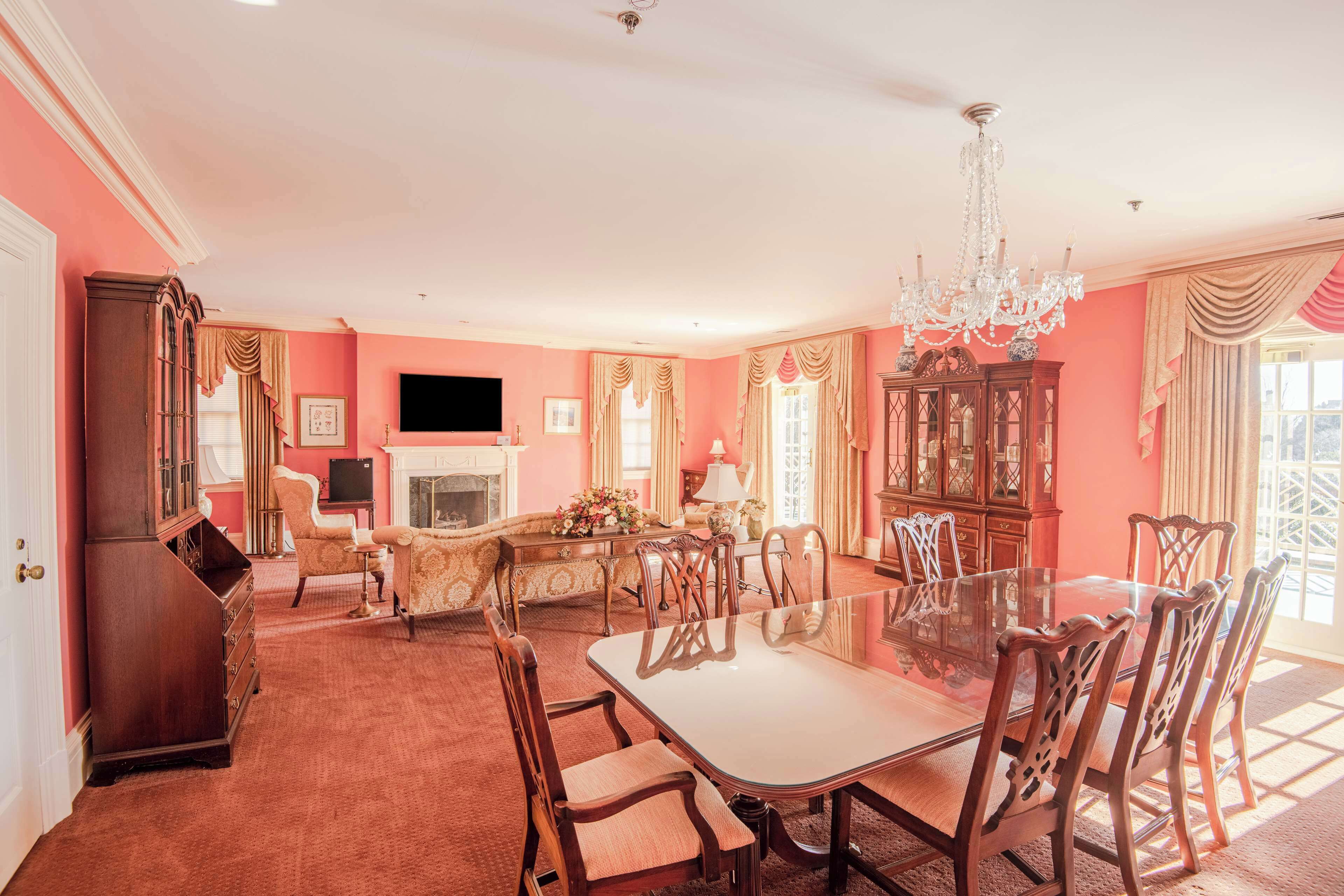 A spacious room with a large dining table, elegant chairs, a chandelier, and a fireplace.