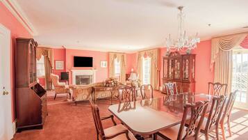 A spacious room with a large dining table, elegant chairs, a chandelier, and a fireplace.