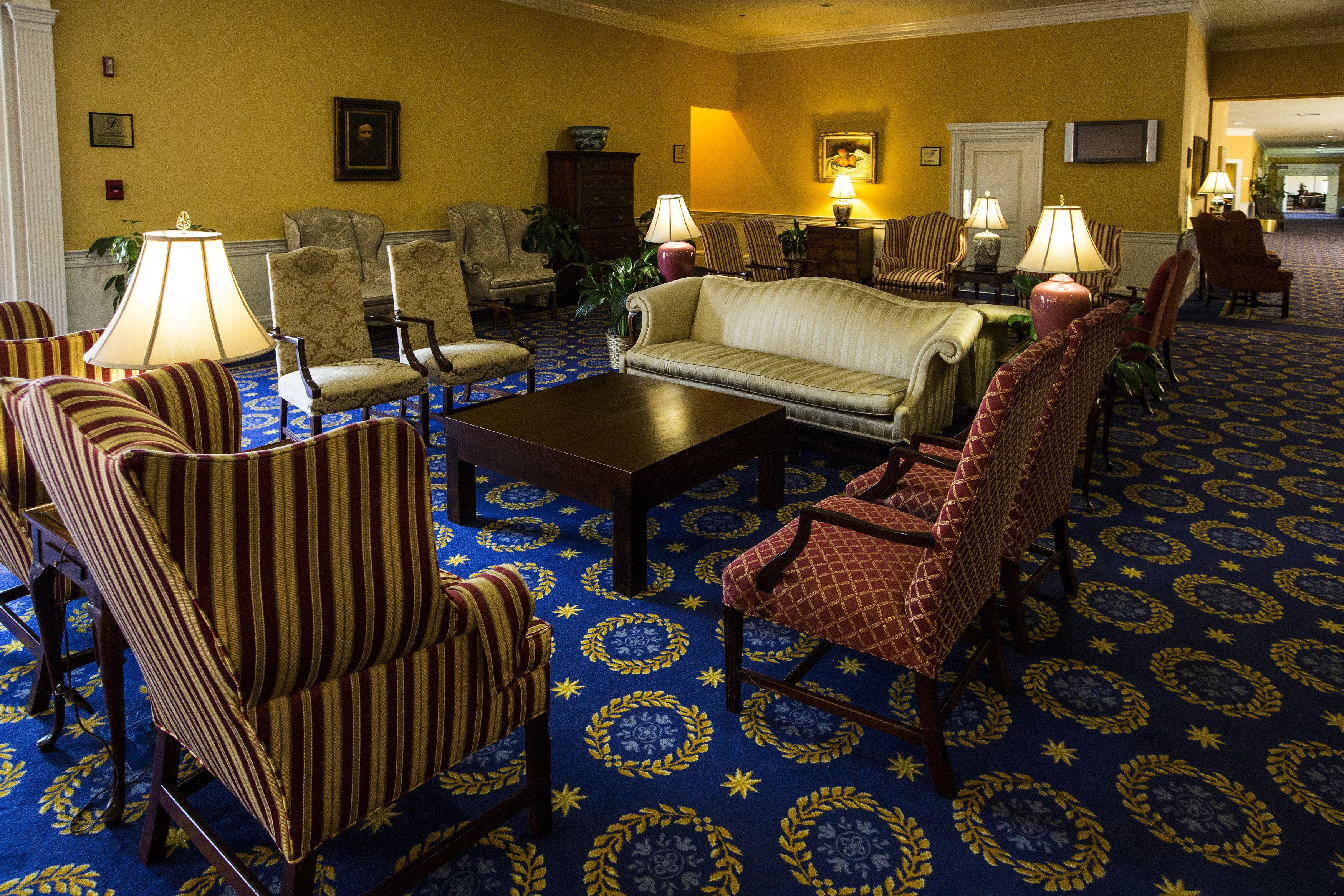 Een hotellobby met een kamerbreed tapijt, meerdere banken, fauteuils en lampen.