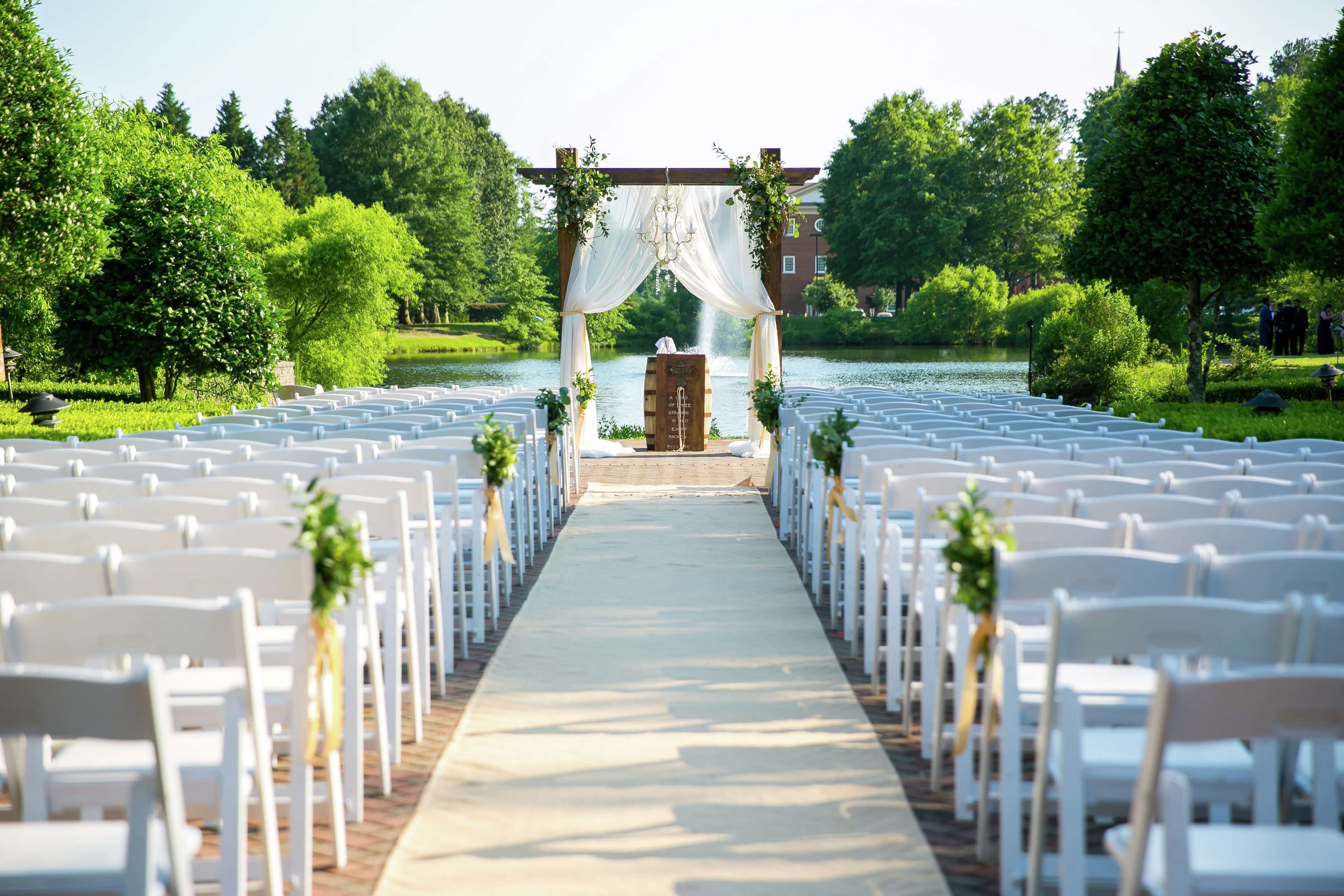 A wedding aisle with white chairs and a wooden archway.