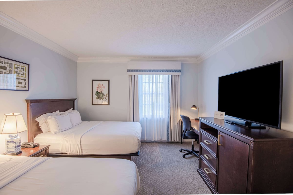 A hotel room with two beds, a desk, a television, and a window with curtains.