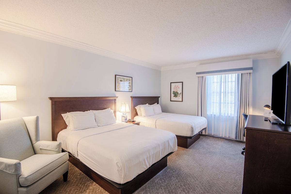 A hotel room with two beds, a desk, a TV, and a chair.