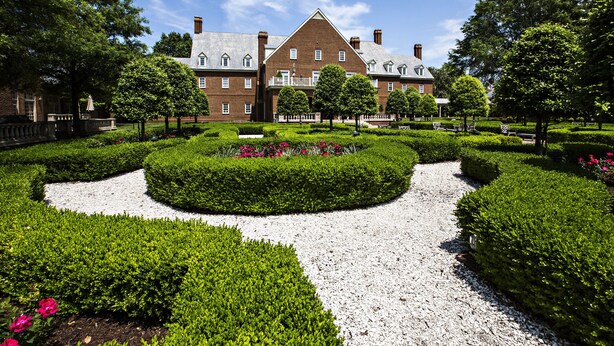 A large brick building with a symmetrical garden layout, including a gravel path and neatly trimmed hedges. - The Founders Inn and Spa, Tapestry Collection by Hilton (Virginia Beach)