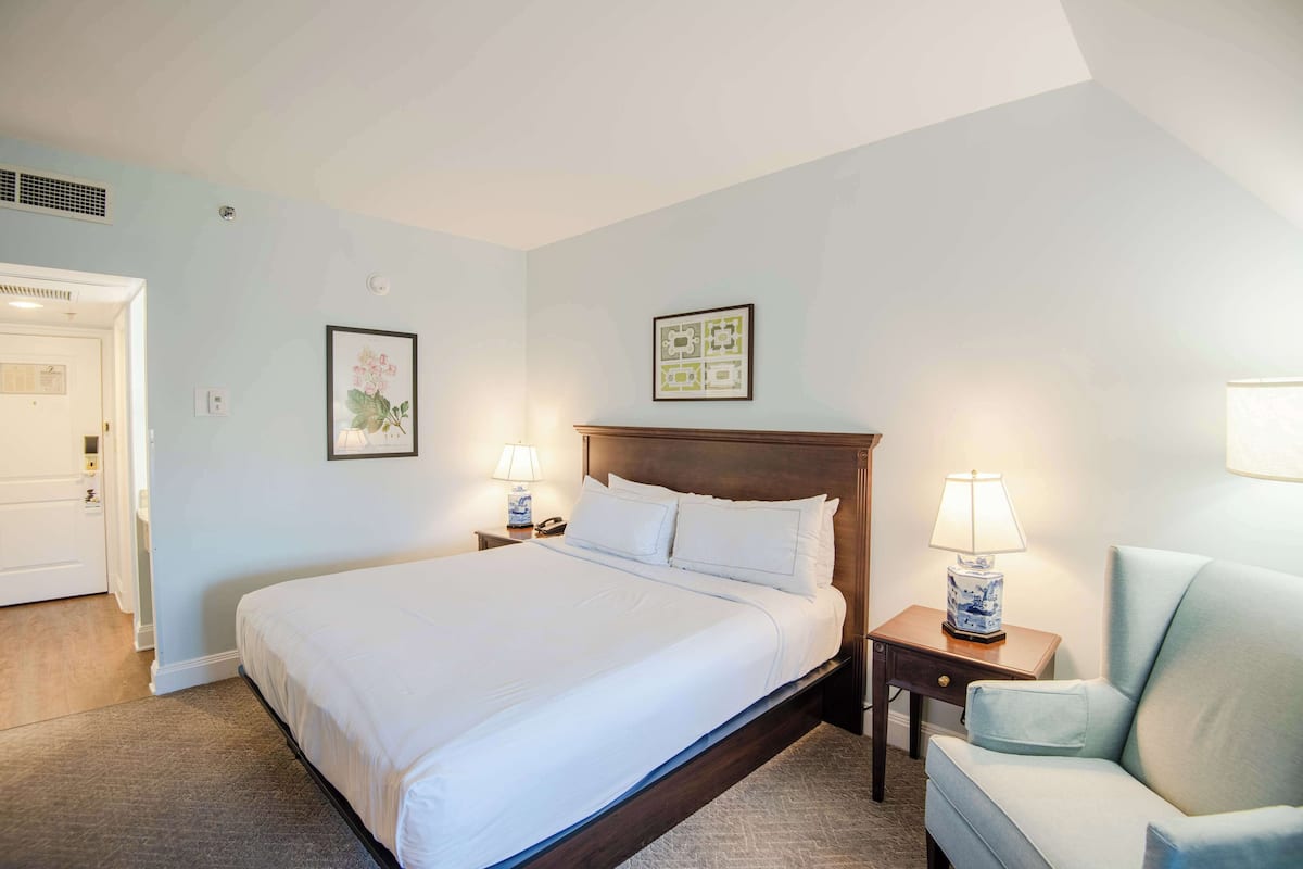 A neatly arranged hotel room with a large bed, bedside tables with lamps, a chair, and framed artwork on the walls.