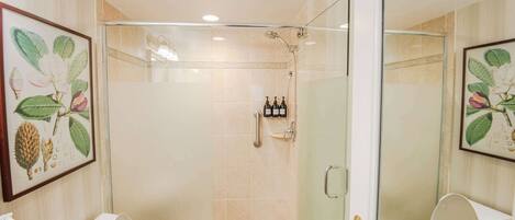 A bathroom with a shower, toilet, and sink. There are framed botanical prints on the walls.