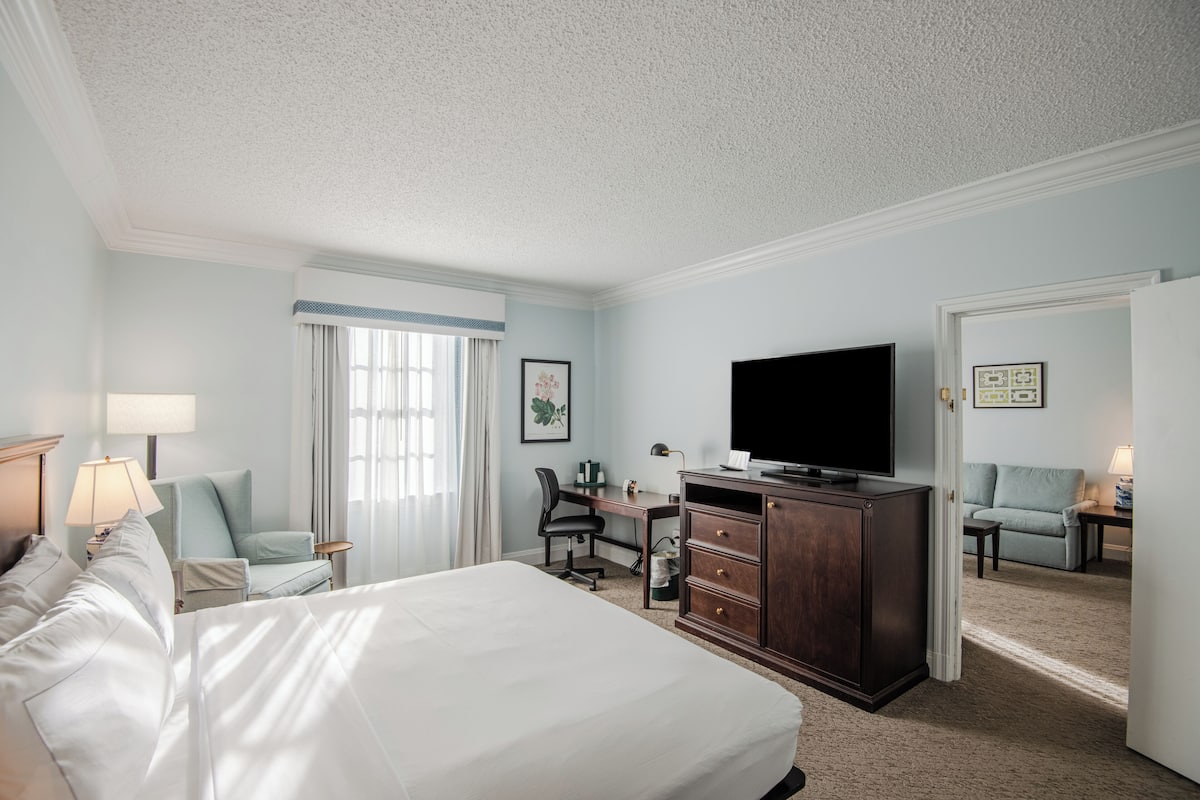 A hotel room with a large bed, a desk with a chair, a television, and a seating area with a sofa and armchairs.