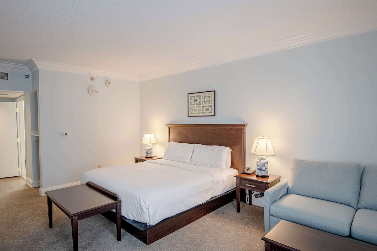 A neatly arranged hotel room with a bed, bedside tables, a chair, and a framed picture on the wall.