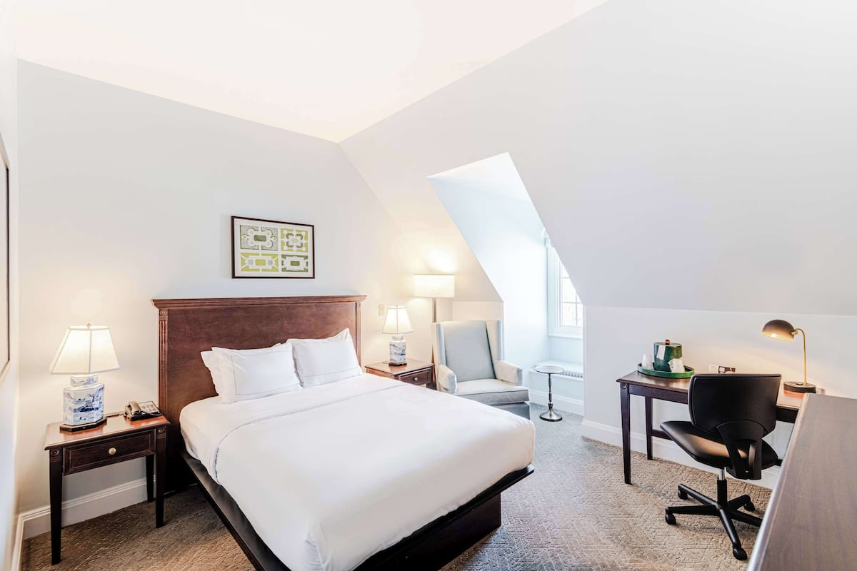 A hotel room with a large bed, two bedside tables with lamps, a desk with a chair, and a small table with a lamp.
