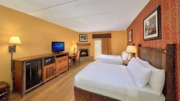 A hotel room with two beds, a television, a fireplace, and a wooden dresser.