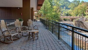 Een overdekt terras met houten stoelen en een tafel, met uitzicht op een rivier en een brug.