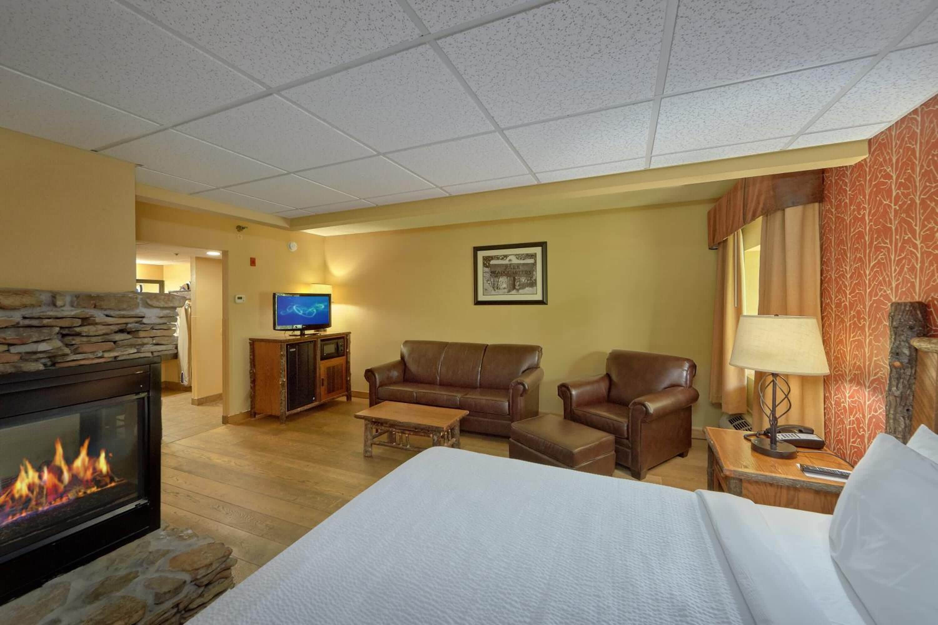 A hotel room with a fireplace, a television, a sofa, a chair, and a bed.