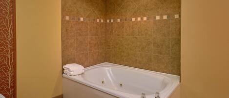 Un baño con una bañera grande, paredes color beige y una zona de ducha con azulejos.