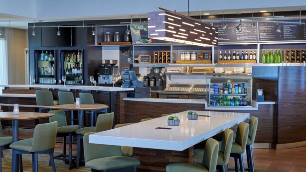 Uma área de bar moderna com um balcão comprido, diversas opções de assento e uma variedade de bebidas e petiscos expostos em prateleiras.