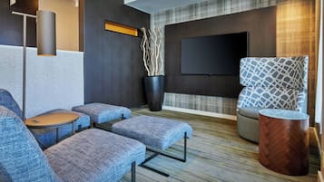 Un espace détente moderne, doté de sièges confortables, d’un téléviseur à écran plat et d’une plante décorative.