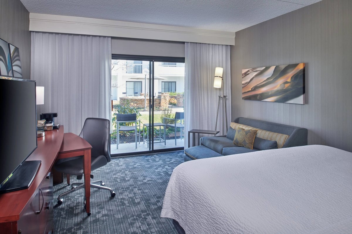 A hotel room with a bed, a desk with a computer, a chair, a sofa, a lamp, and a painting on the wall.