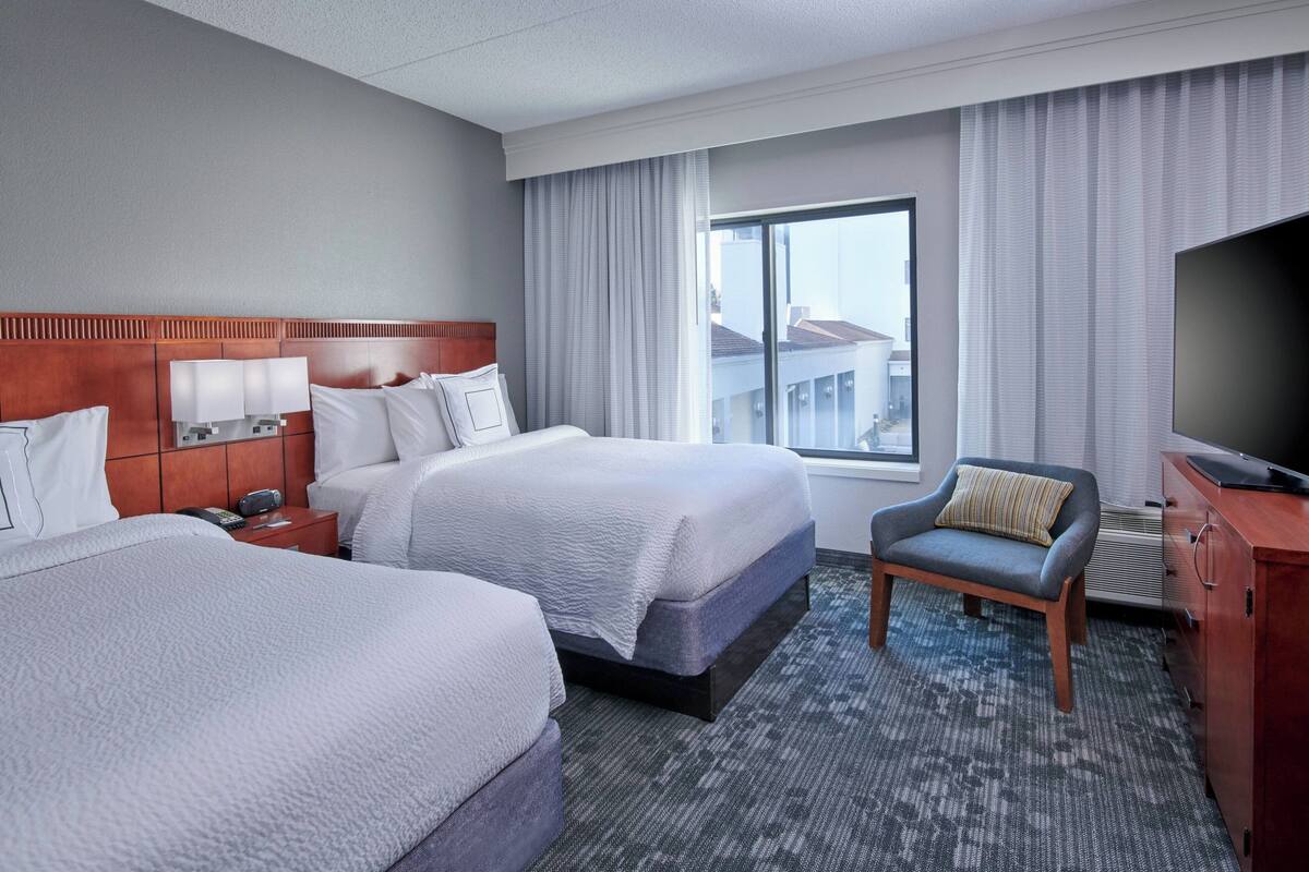 A hotel room with two beds, a TV, a desk, and a chair.