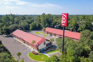 Un hotel Red Roof Inn con estacionamiento, un edificio de techo rojo y follaje circundante.