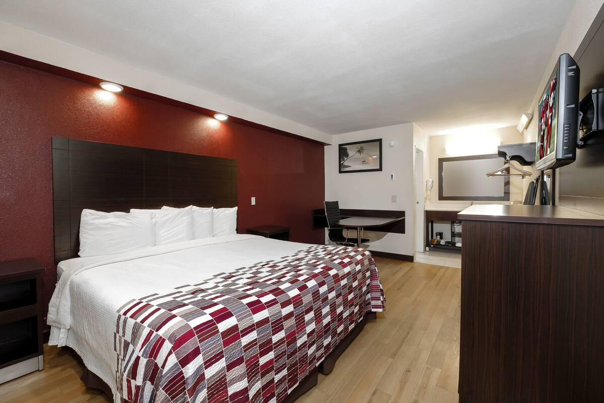 A hotel room with a large bed, a desk, a chair, a mirror, and a TV.