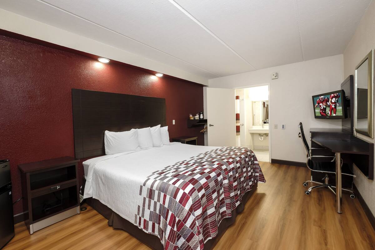 A hotel room with a large bed, a desk with a chair, a TV mounted on the wall, and a wardrobe.