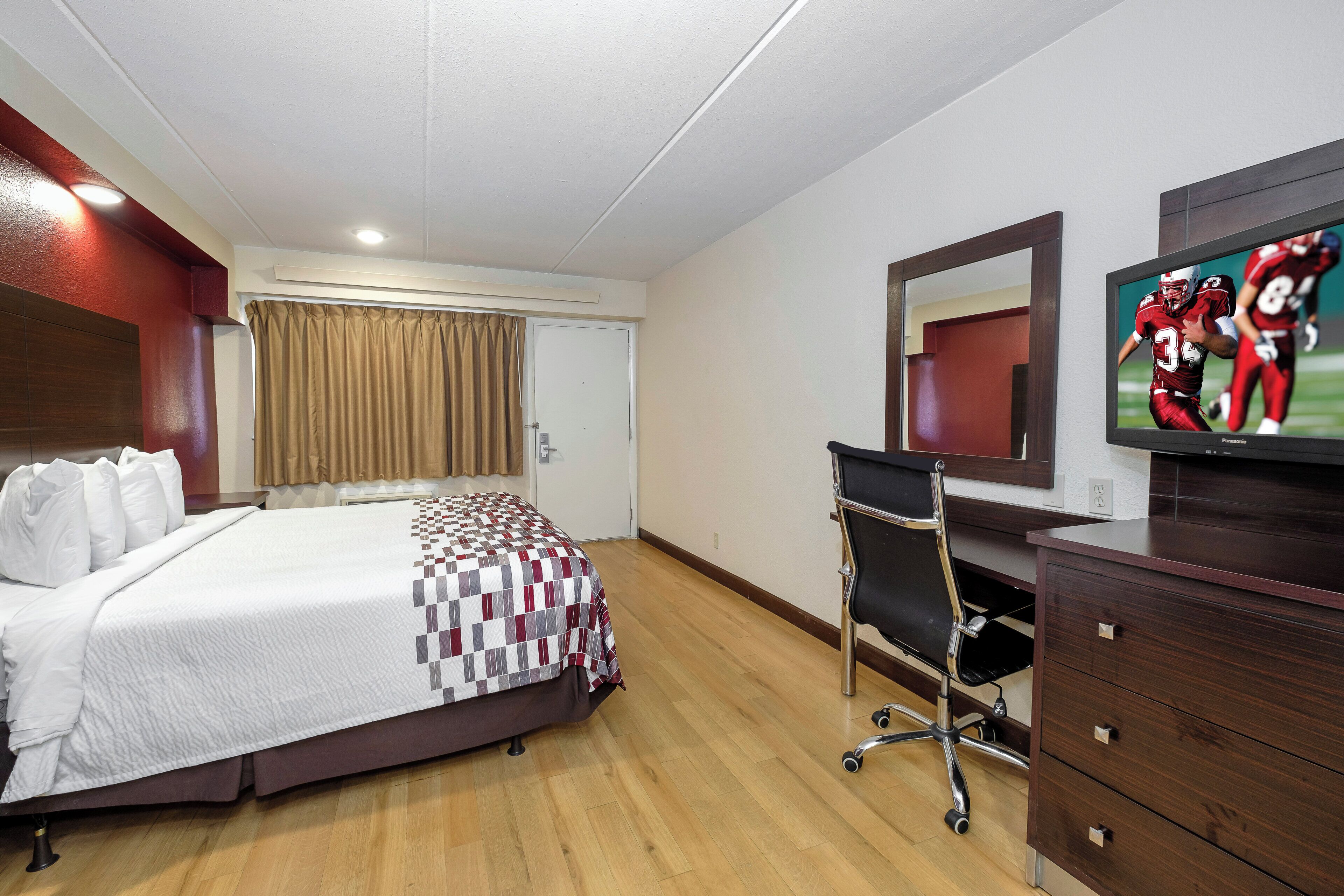 A hotel room with a bed, a desk, a chair, a television, and a mirror.
