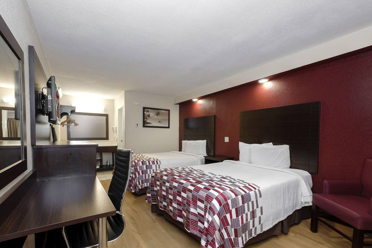 A hotel room with two beds, a desk, a chair, and a TV.