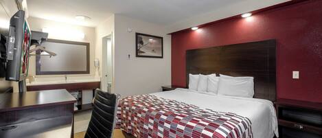 A hotel room with a bed, a desk with a chair, a TV, a mirror, and a painting on the wall.