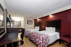 Habitación de hotel con dos camas, un escritorio, una silla, un televisor y una pared de acento roja.