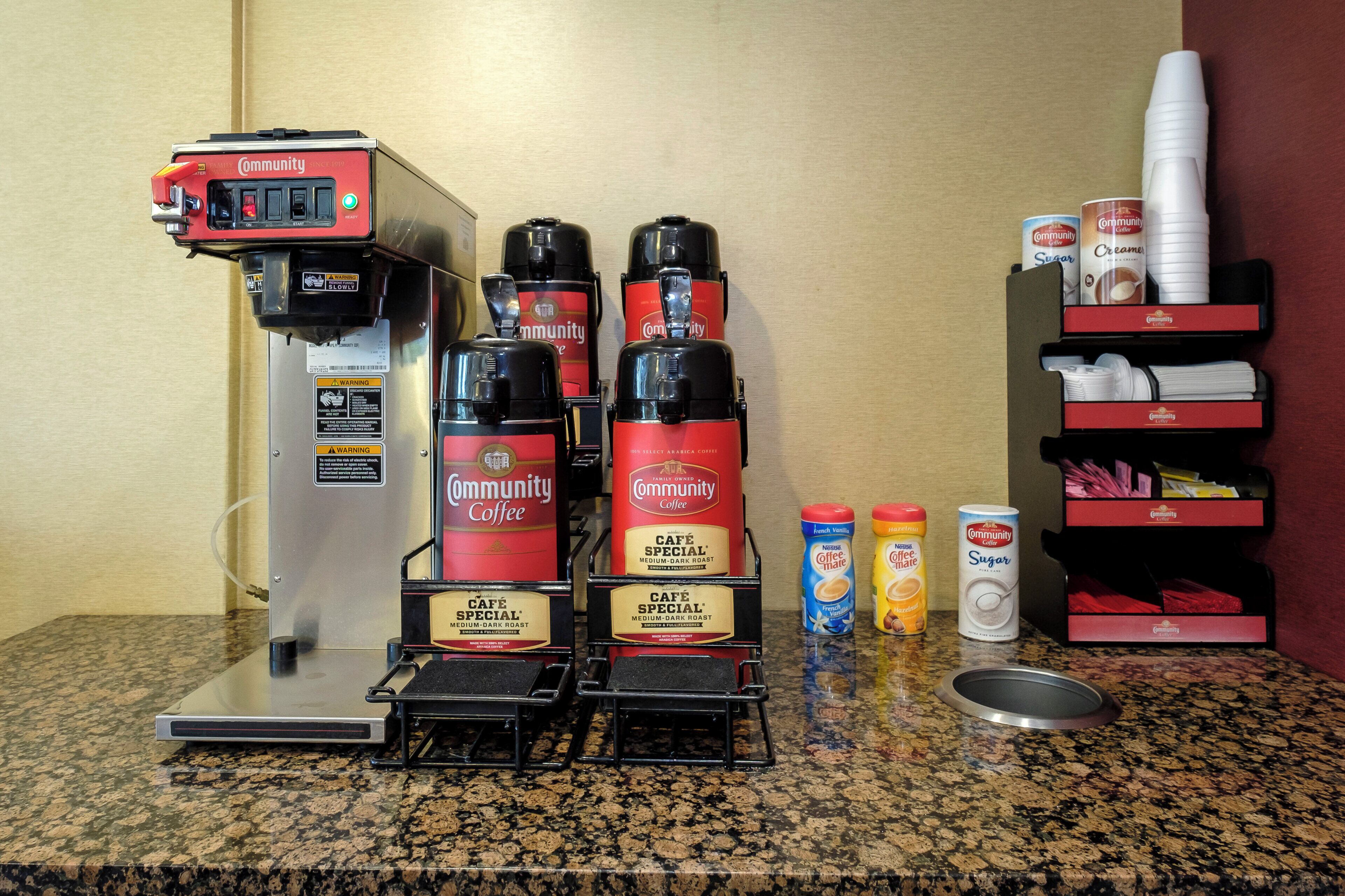 A coffee station with a coffee machine, multiple coffee dispensers, and a selection of coffee creamer and sugar.
