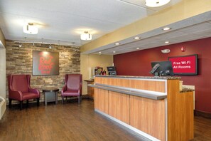 A hotel reception area with a stone wall, two red chairs, a wooden reception desk, and a sign indicating free Wi-Fi in all rooms. - Red Roof Inn Tallahassee - University (Tallahassee)