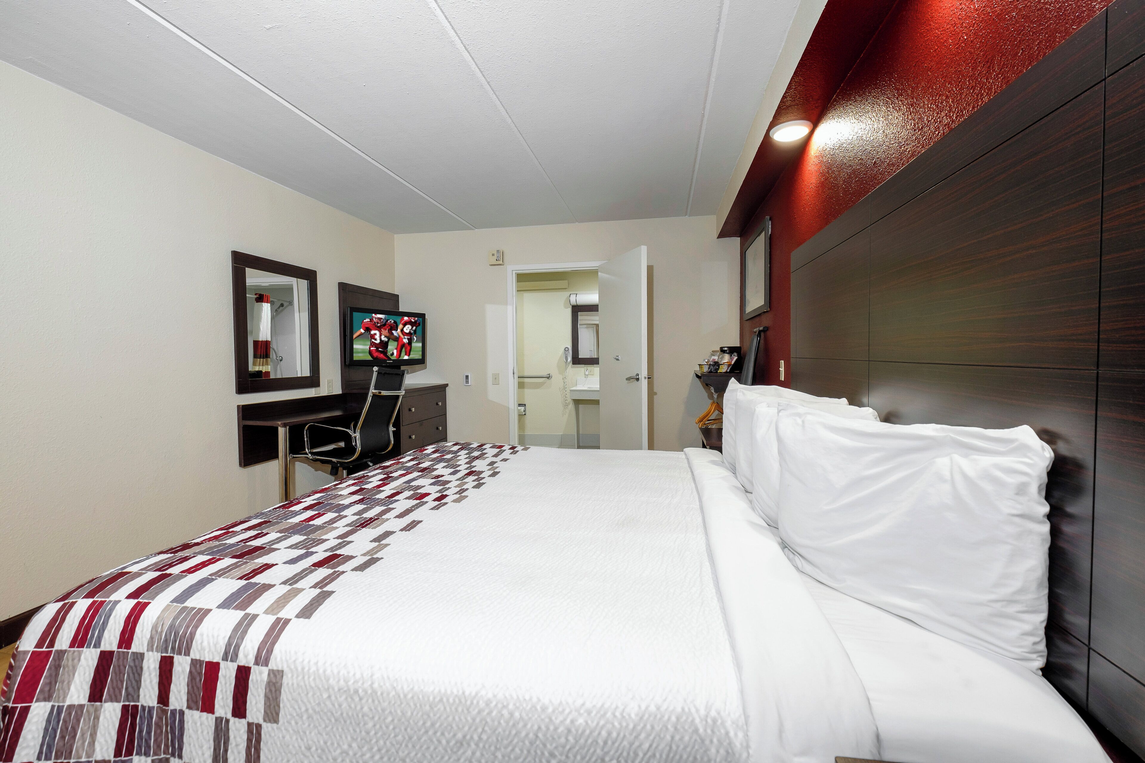 A hotel room with a bed, a desk, a mirror, and a television.